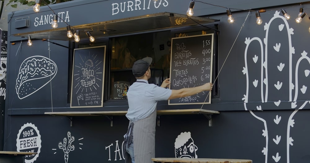 Mężczyzna w fartuchu przy ladzie czarnego food trucka